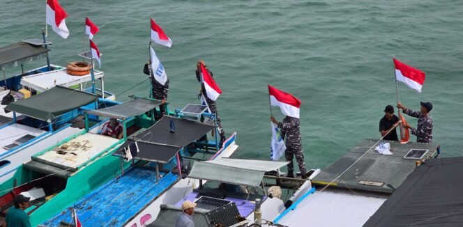 
					Prajurit TNI AL memasangkan bendera merah putih di sejumlah perahu nelayan di perairan tapal batas RI - Malaysia di Karang Unarang jelang HUT 80 RI. Dok.Penerangan LANAL Nunukan.